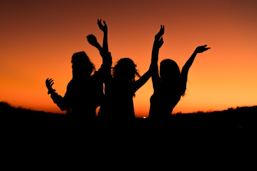 Silhouettes of three people dancing and celebrating at sunset