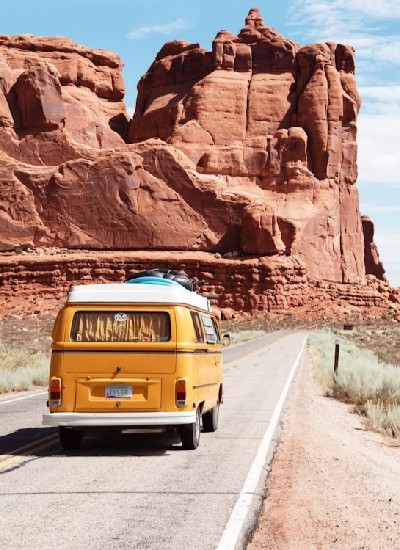 Fourgon jaune roulant sur une route désertique avec des formations rocheuses rouges en arrière-plan