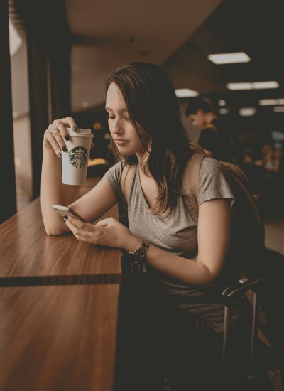 Jonge vrouw die in een café zit, koffie drinkt en op haar telefoon kijkt